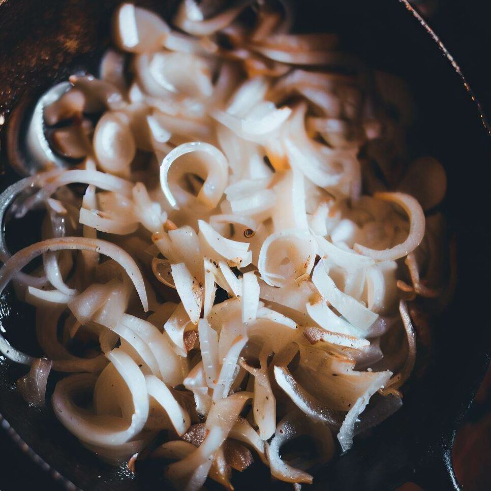 Photo of thinly sliced white onions sautéing in an iron skillet